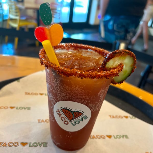 A Taco Love Michelada with a chili-lime rim, cucumber slice, and cactus-themed stirrer.