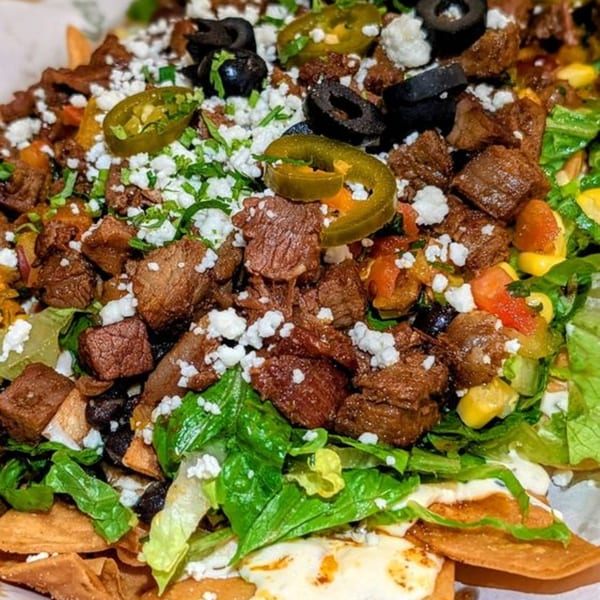 Close-up of Taco Love's loaded nachos with steak, jalapeños, olives, crumbled cheese, and lettuce.