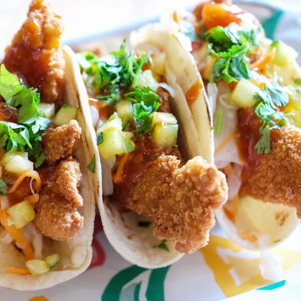 Three crispy chicken tacos with salsa, cilantro, and diced pineapple on a colorful plate.