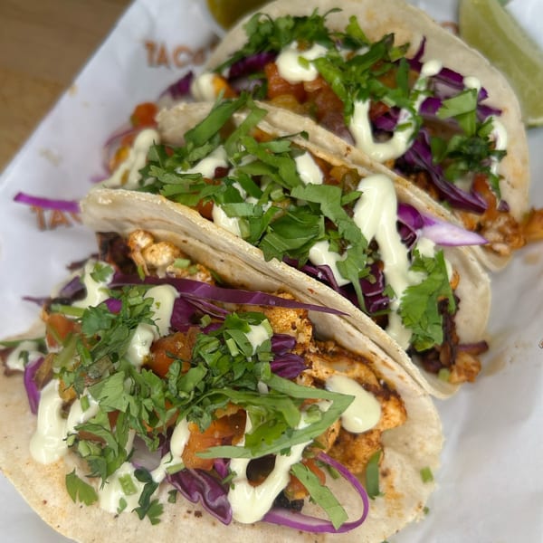 Three vibrant Taco Love tacos with red cabbage, cilantro, and crema, served with lime.