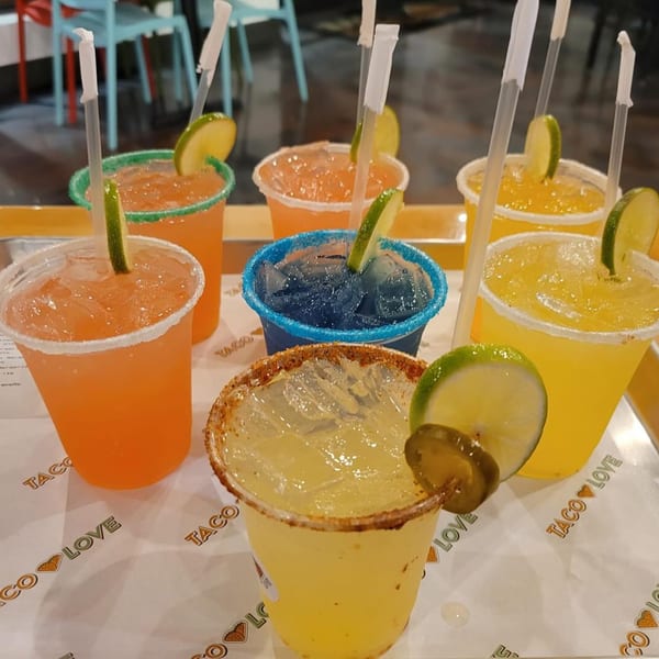 A tray of colorful margaritas from Taco Love, garnished with lime and some with jalapeños.