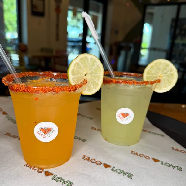 Two Taco Love margaritas, one orange and one green, with chili-lime rims and lime slices.
