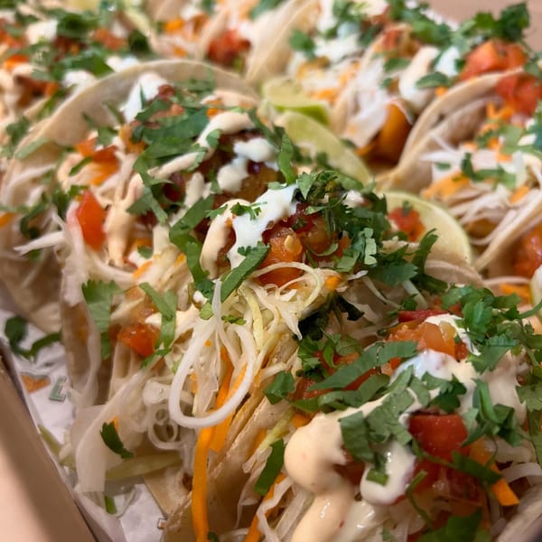 Close-up of multiple Taco Love tacos with shredded cabbage, tomatoes, cilantro, and sauces.