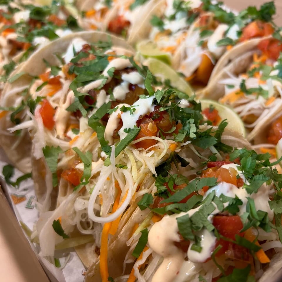 Close-up of multiple Taco Love tacos with shredded cabbage, tomatoes, cilantro, and sauces.