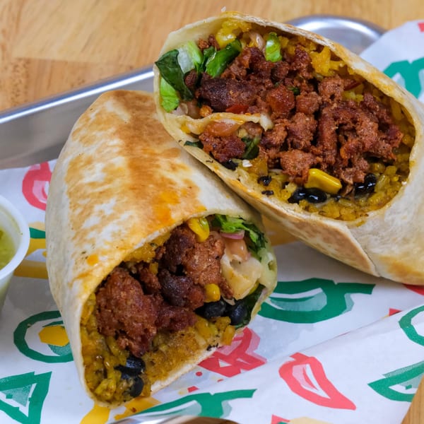 Two halves of a large, cut burrito filled with meat, rice, beans, and vegetables on a tray.