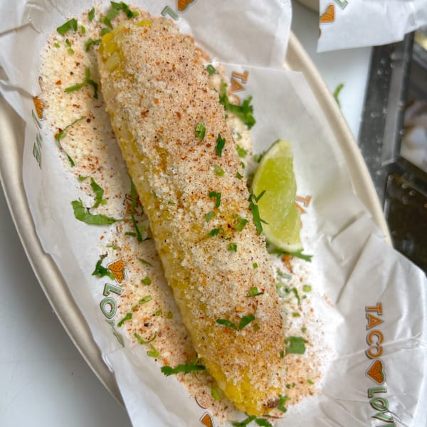 Elote, Mexican street corn, topped with cheese, chili powder, and cilantro, with a lime wedge.